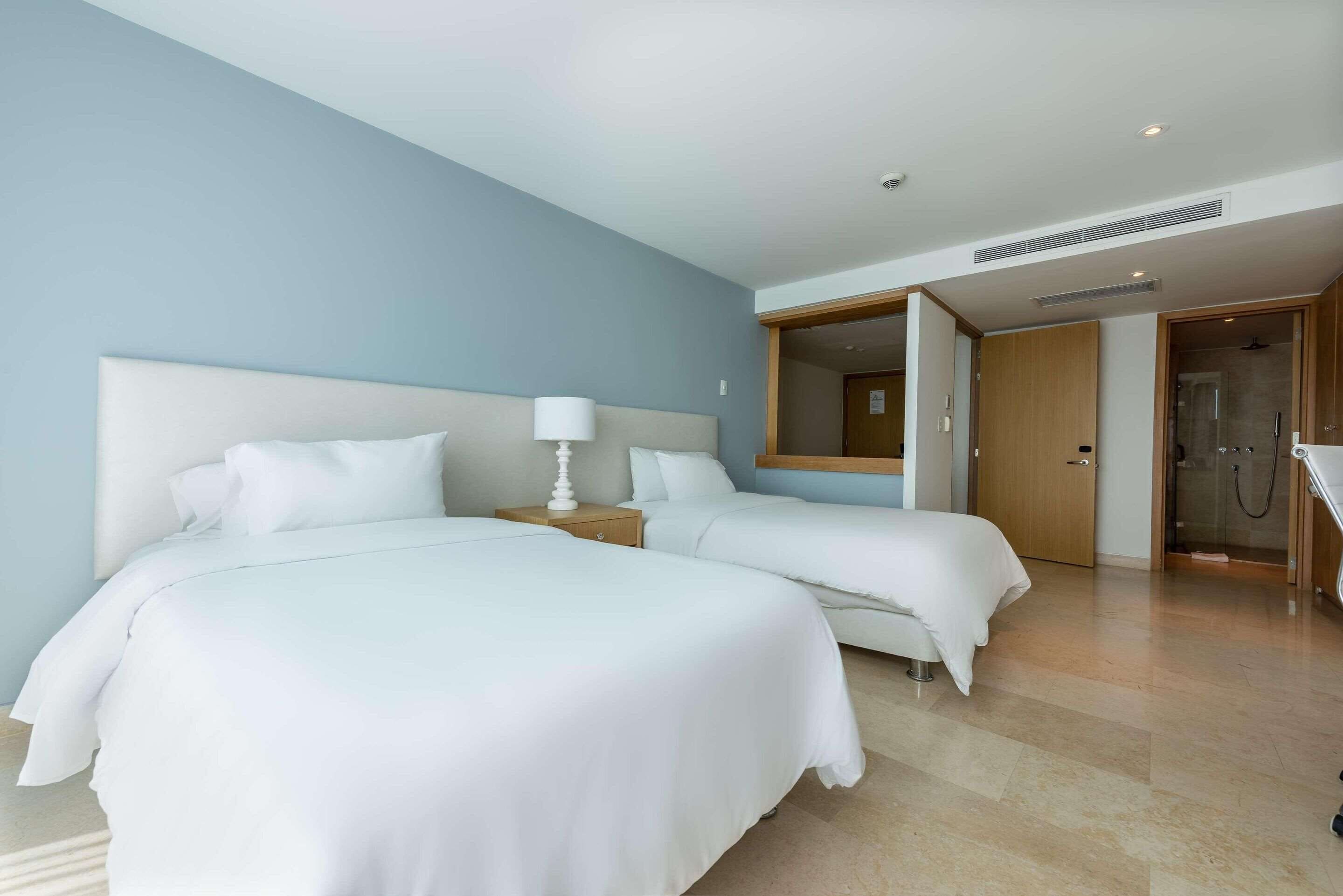 A hotel room with two beds, a large mirror, and a shower area.
