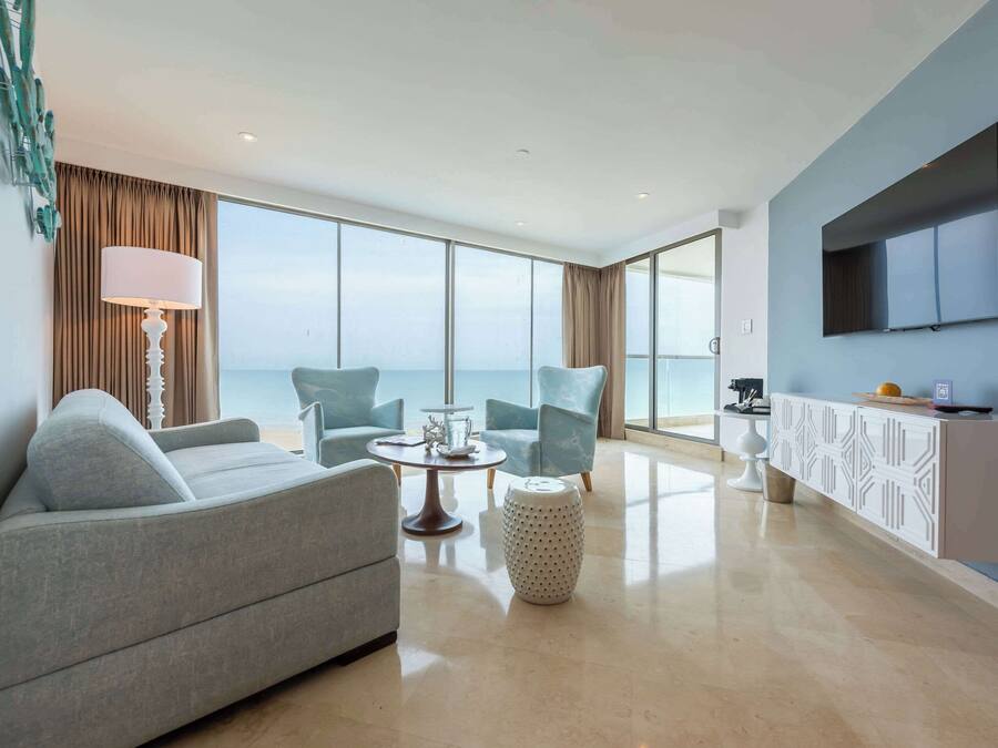 A modern living room with a sofa, two armchairs, a coffee table, and a TV mounted on the wall.