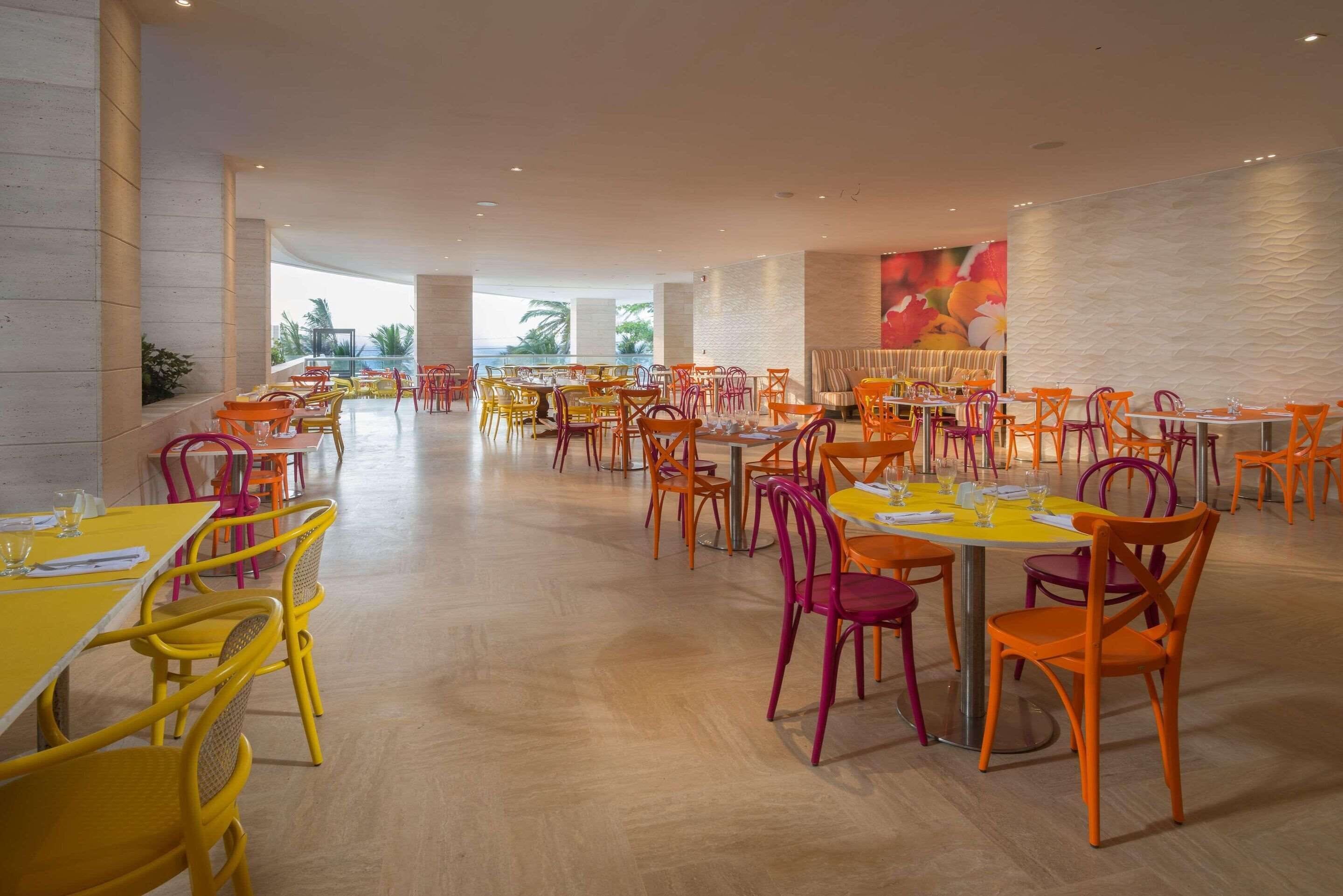 Een ruime eethoek met meerdere tafels en stoelen, grote ramen en een modern interieur.