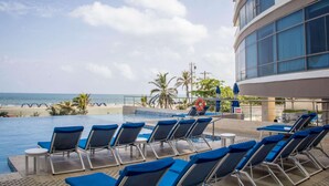 Zona de piscina con sillones de descanso y vista a la playa y el océano.