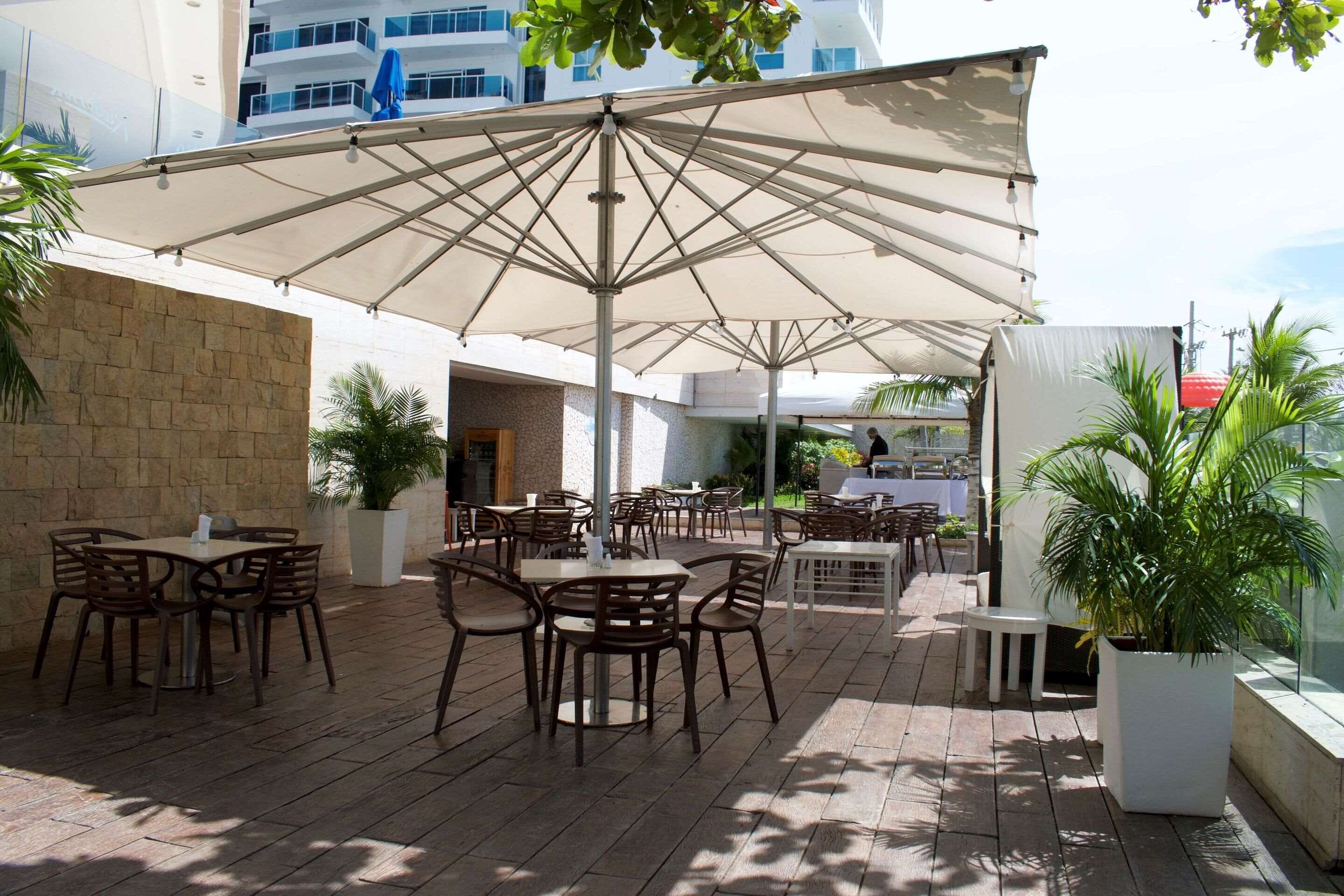 An outdoor patio area with tables and chairs, a large umbrella, and potted plants.