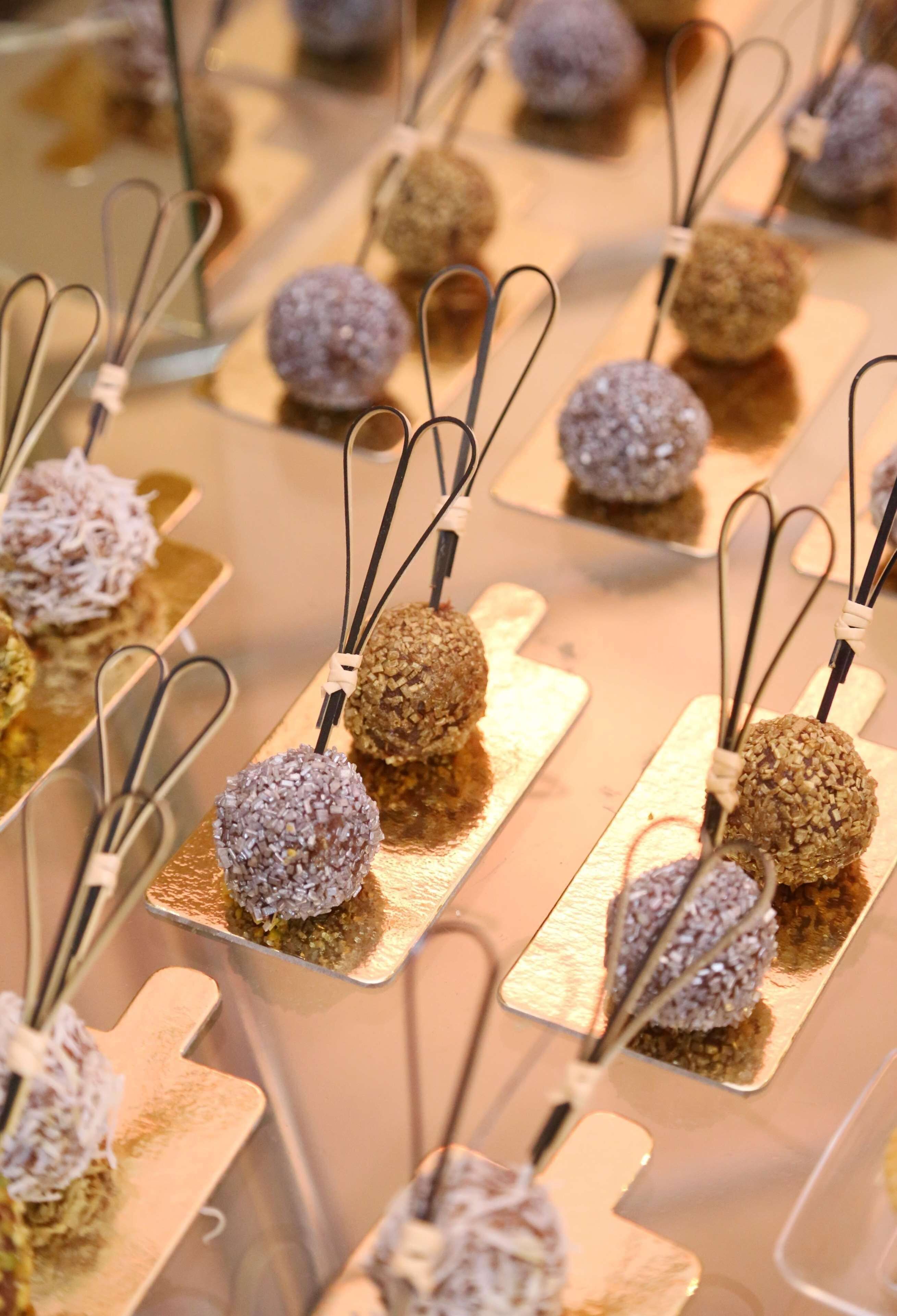 A display of spherical treats on rectangular bases with metal hooks, arranged on a reflective surface.
