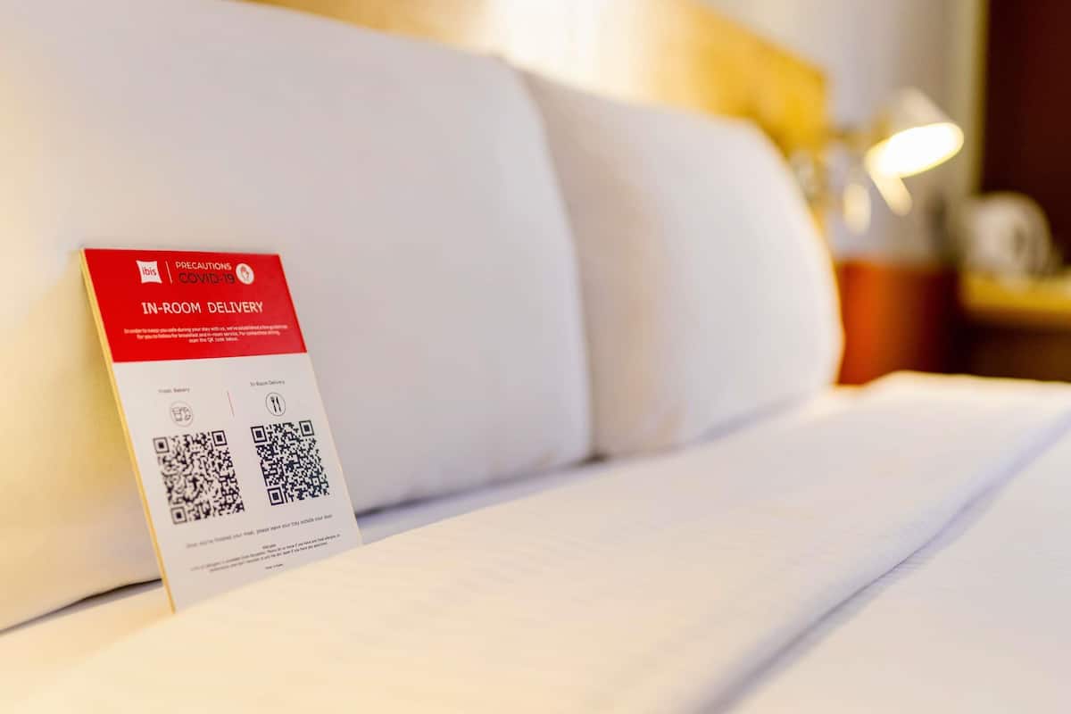 A hotel room with a bed, a pillow, and a sign indicating in-room delivery services.