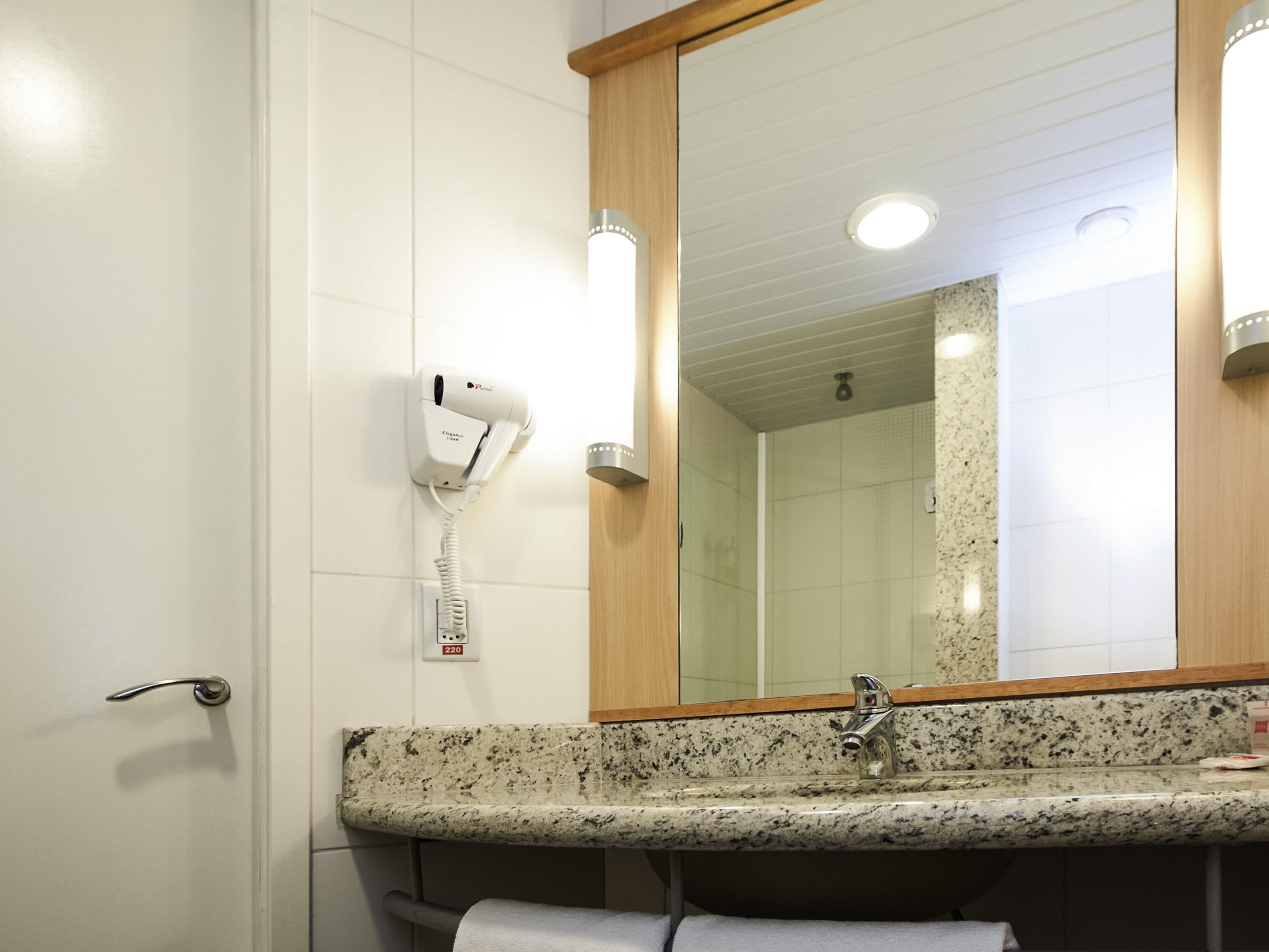 A bathroom with a sink, mirror, towel rack, and a hairdryer mounted on the wall.