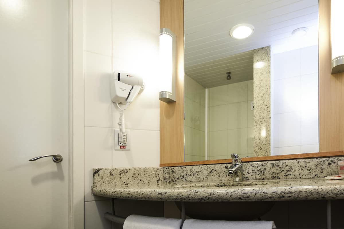 Un baño con lavamanos, espejo, toallero y secador de pelo montado en la pared.