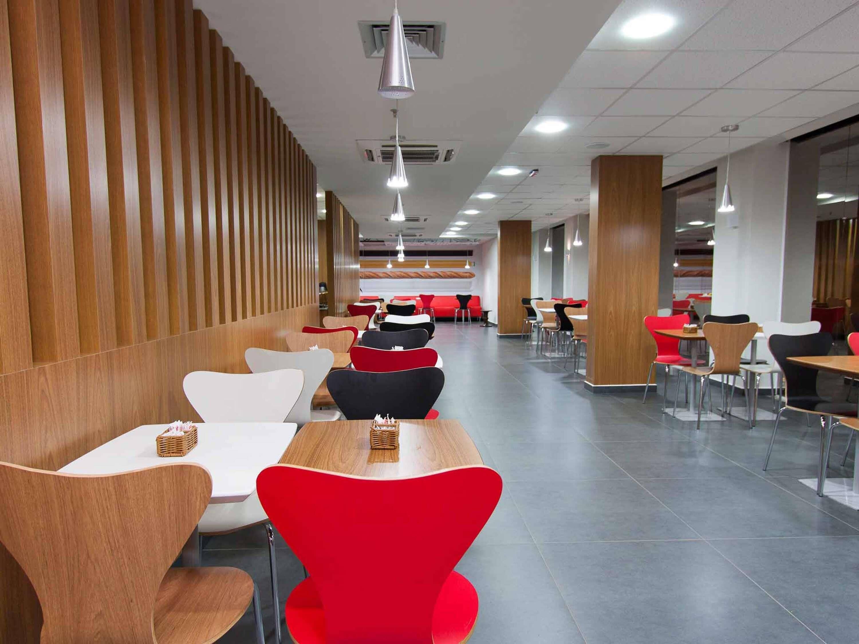 Une cafétéria moderne avec des murs recouverts de panneaux de bois, des chaises rouges et blanches, et de nombreuses tables.