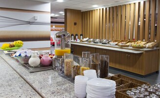 Zona de bufé con diversas opciones de comida, un dispensador de jugo y una máquina de café.