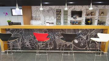 A bar area with a wooden counter, black and white patterned wall, and four bar stools, one red and three white.