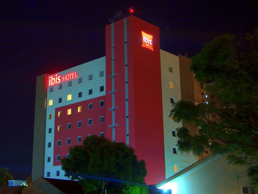 Un hotel con fachada roja y blanca, varios pisos y un llamativo letrero de 'ibis' en la parte superior.