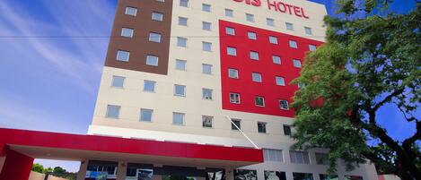 Un hotel con fachada roja y blanca, varios pisos y una zona de entrada techada.