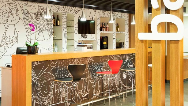 Un espace bar moderne avec un comptoir en bois, des tabourets de bar et un mur orné de dessins abstraits.