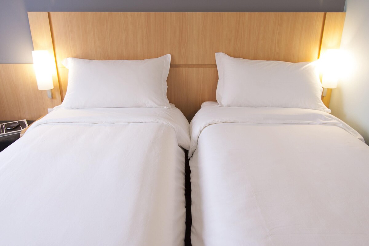 A double bed with white linens and a wooden headboard.