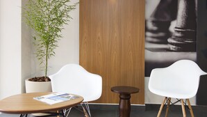 Une pièce moderne avec une porte en bois, deux chaises blanches, une petite table ronde et un pot de bambou.
