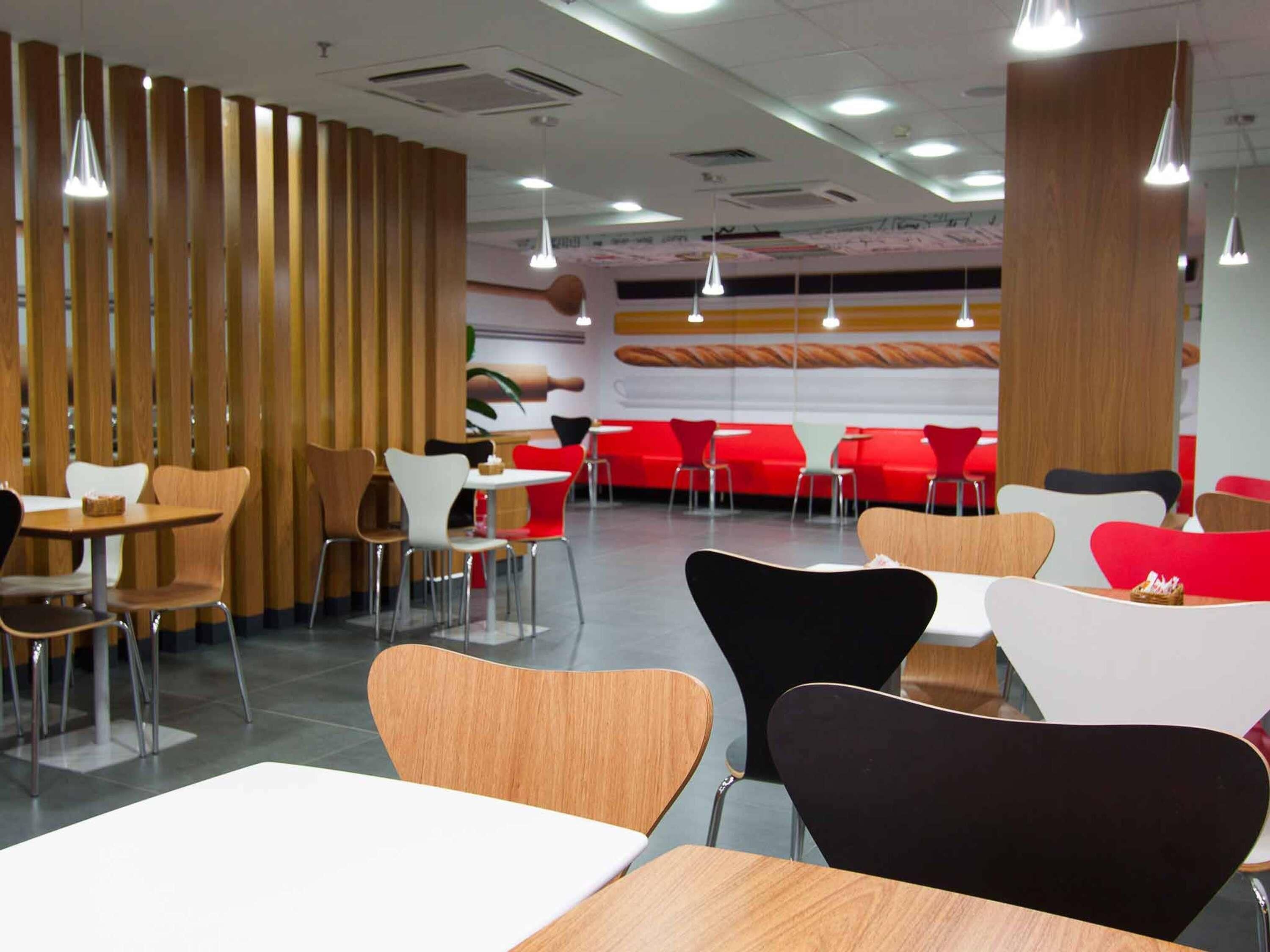 Un interior de restaurante moderno con separadores de madera, asientos de color rojo y blanco, e iluminación colgante.