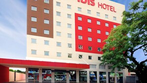 Un hôtel moderne, caractérisé par une façade rouge et beige bien visible, de nombreuses fenêtres et un hall d’entrée facilement identifiable.