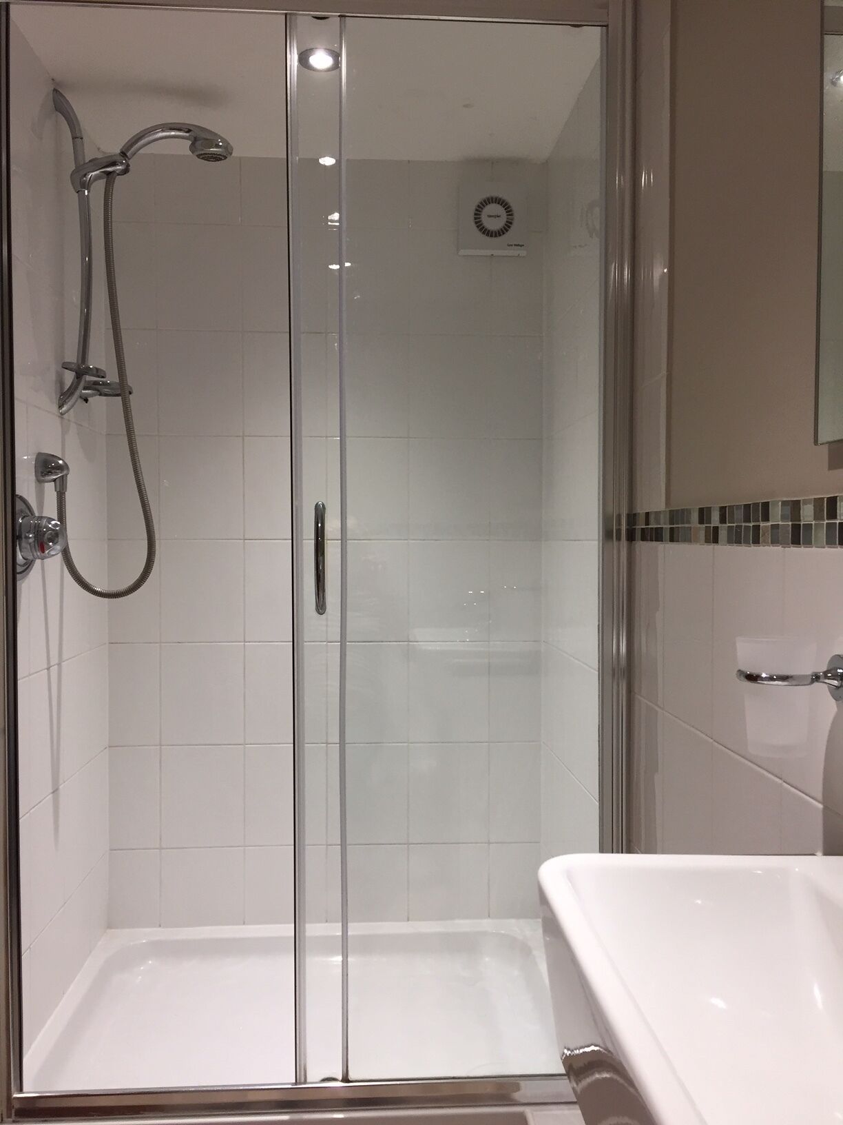 A glass-enclosed shower area with a handheld showerhead and a wall-mounted faucet.