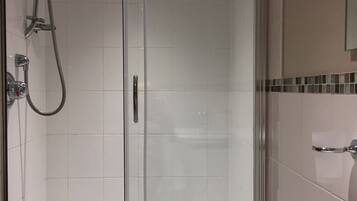 A glass-enclosed shower area with a handheld showerhead and a wall-mounted faucet.