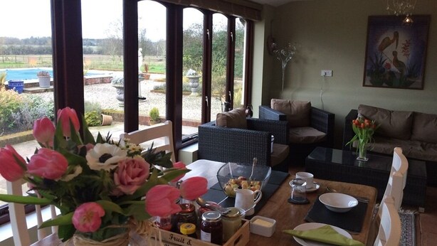 A dining area with a table set for two, a vase of flowers, and a view of the outdoors. - Hazel Barn B&B (Diss)