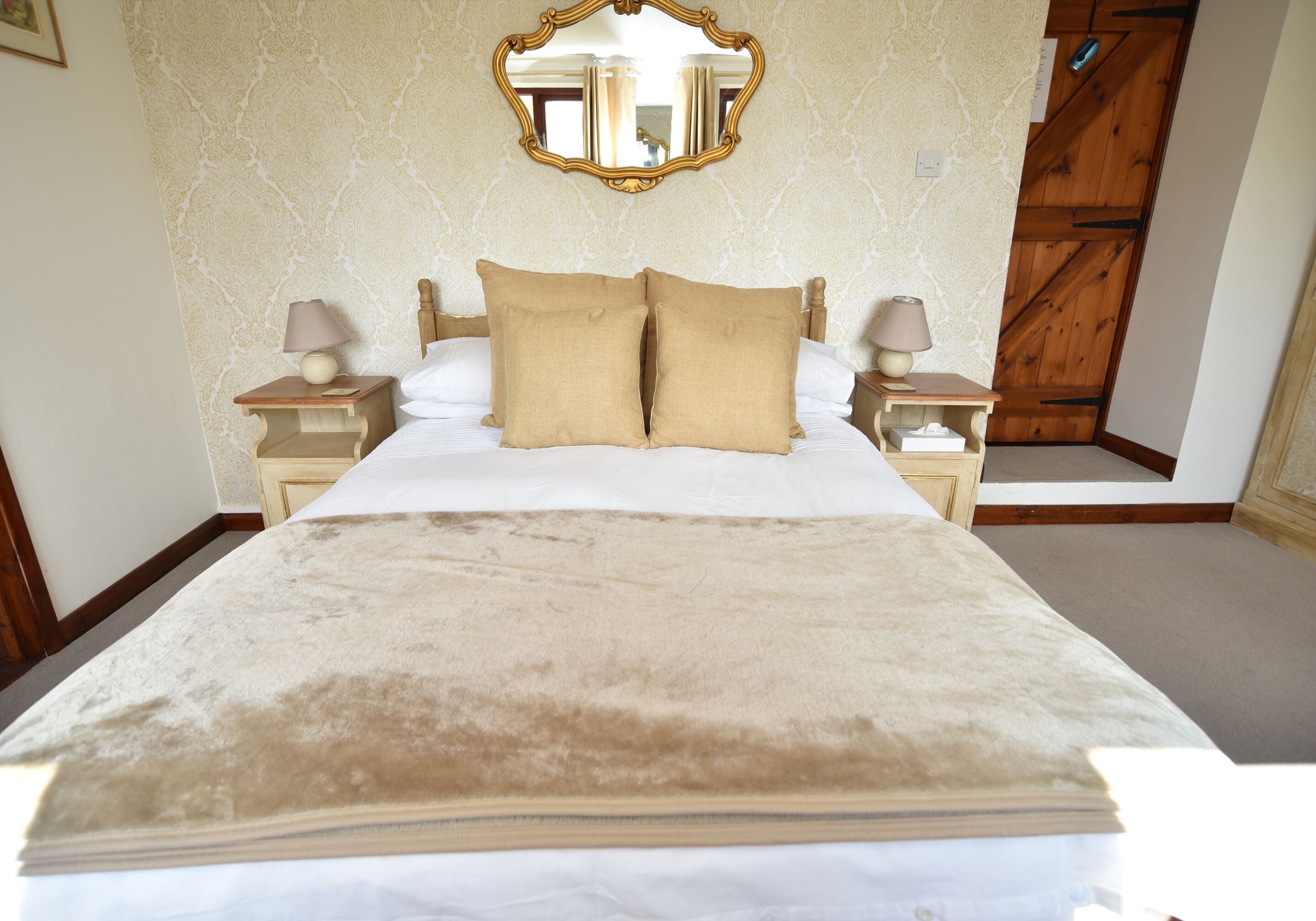 A neatly made bed with a beige blanket, two bedside tables with lamps, and a mirror above the bed.