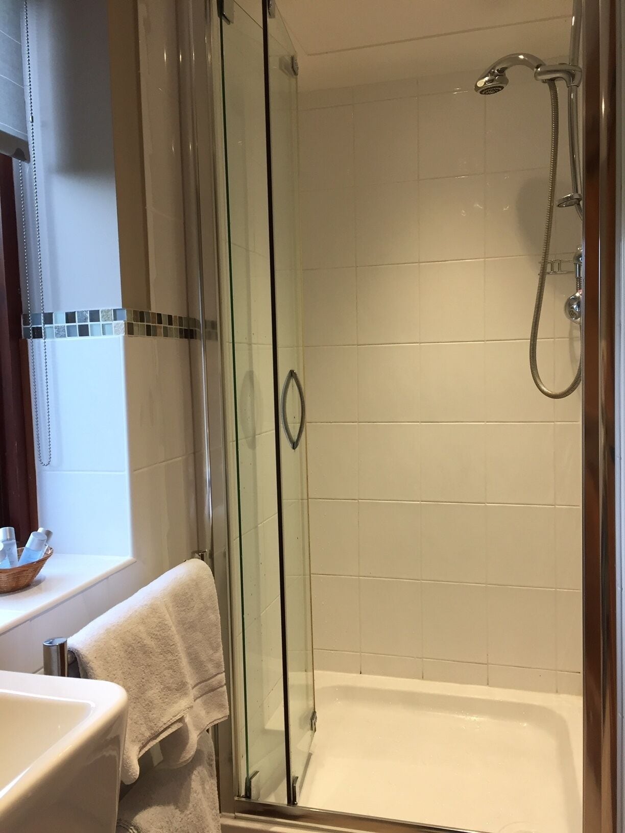 A glass-enclosed shower with a handheld showerhead and a bathtub.