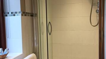 A glass-enclosed shower with a handheld showerhead and a bathtub.