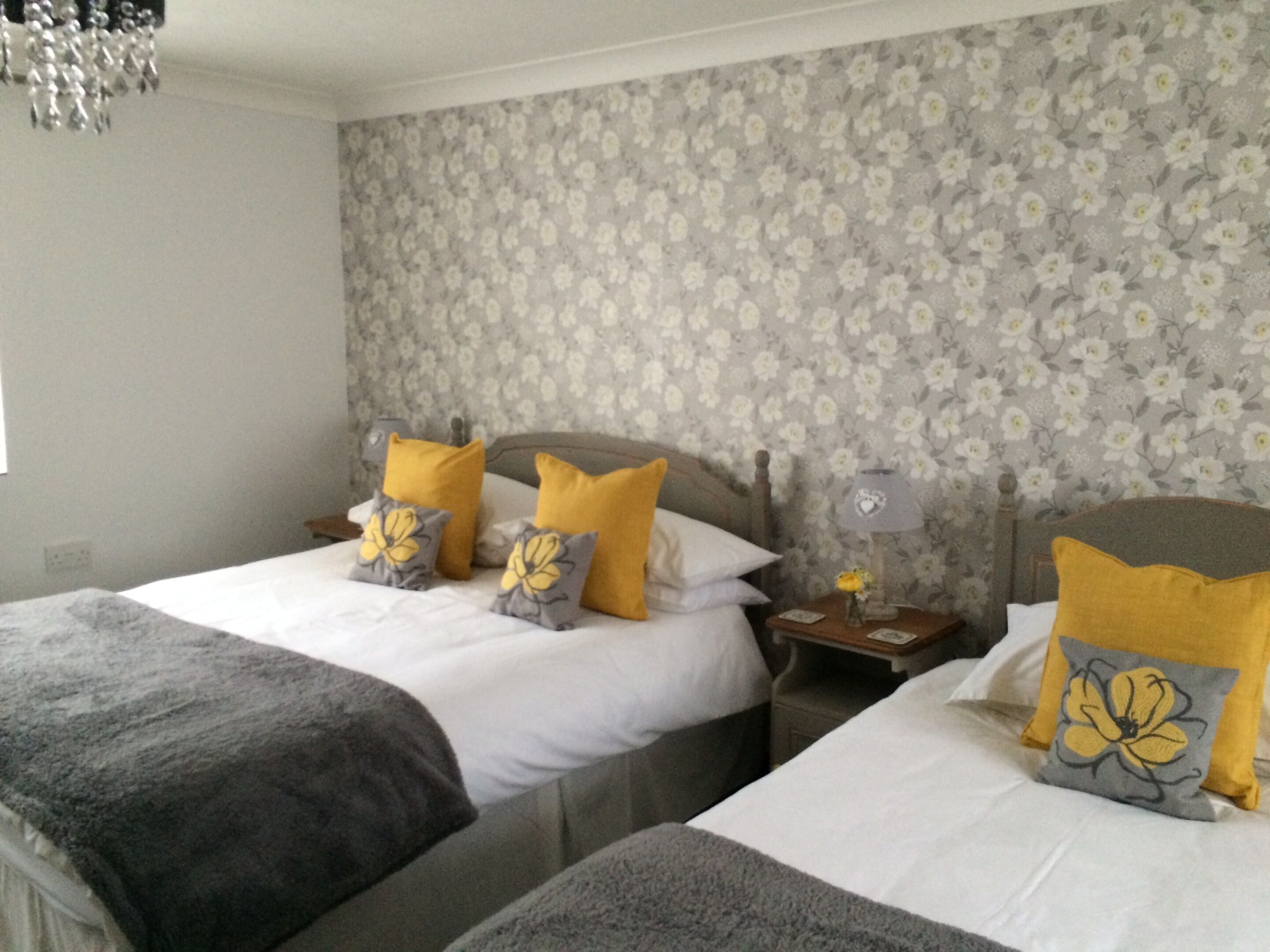 A bedroom with two beds, floral wallpaper, and a nightstand with a lamp.