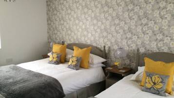 A bedroom with two beds, floral wallpaper, and a nightstand with a lamp.