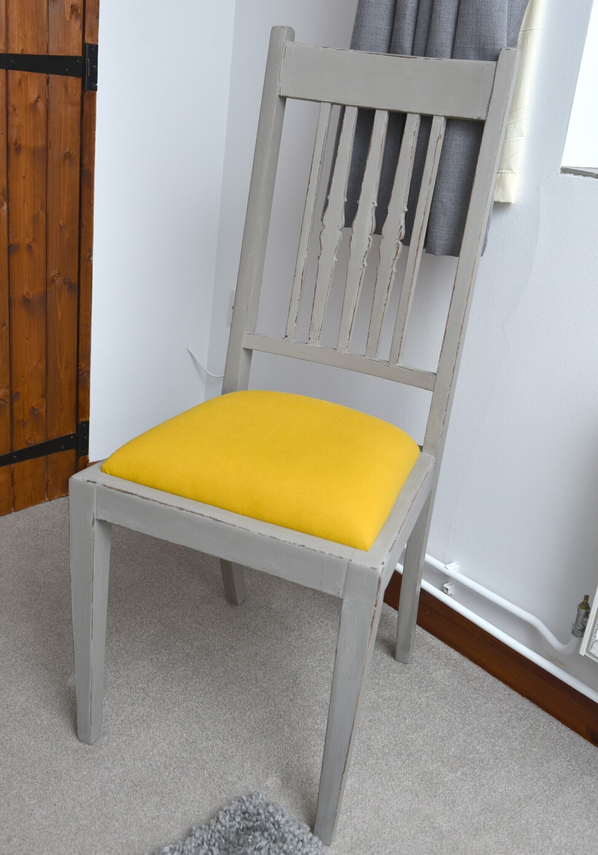 Una silla con cojín amarillo y estructura blanca, sobre piso alfombrado.