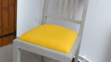 Una silla con cojín amarillo y estructura blanca, sobre piso alfombrado.