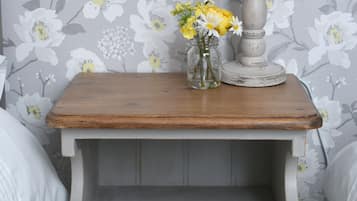 A small wooden nightstand with a drawer, a vase with flowers, and a candle.