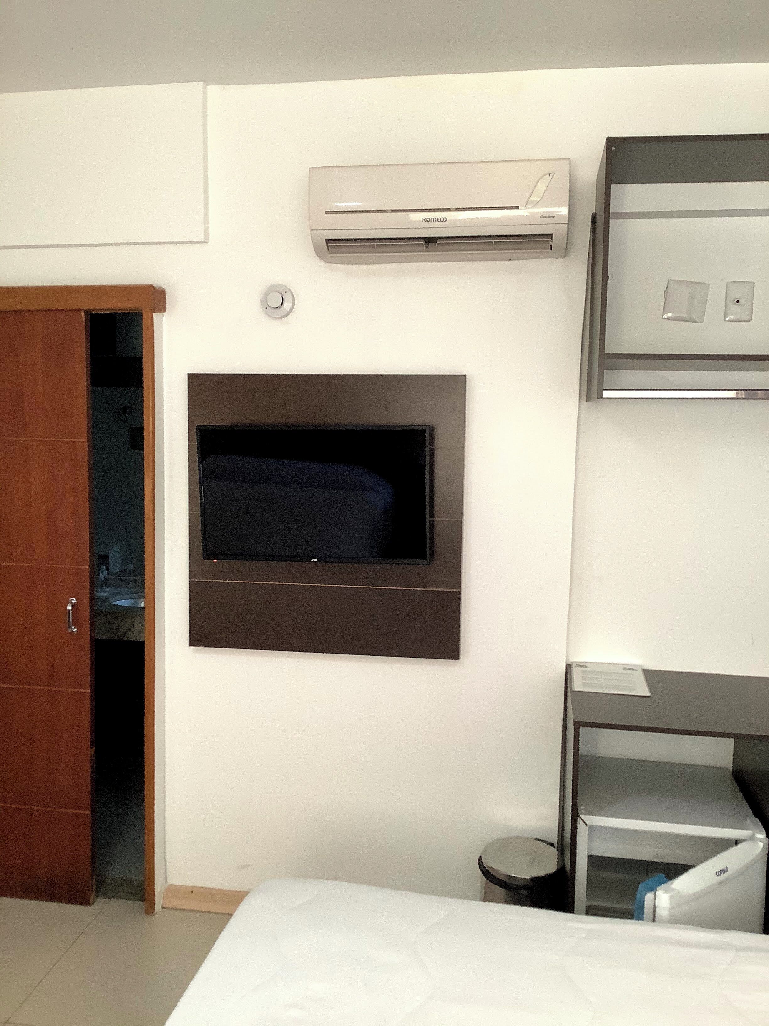 A hotel room with a flat-screen TV mounted on the wall, a minibar, and a wooden wardrobe.