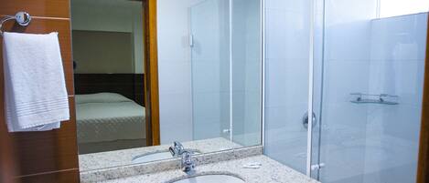 Een moderne badkamer met een granieten wastafel, een grote spiegel, een handdoekhouder en een douche met glazen wanden.