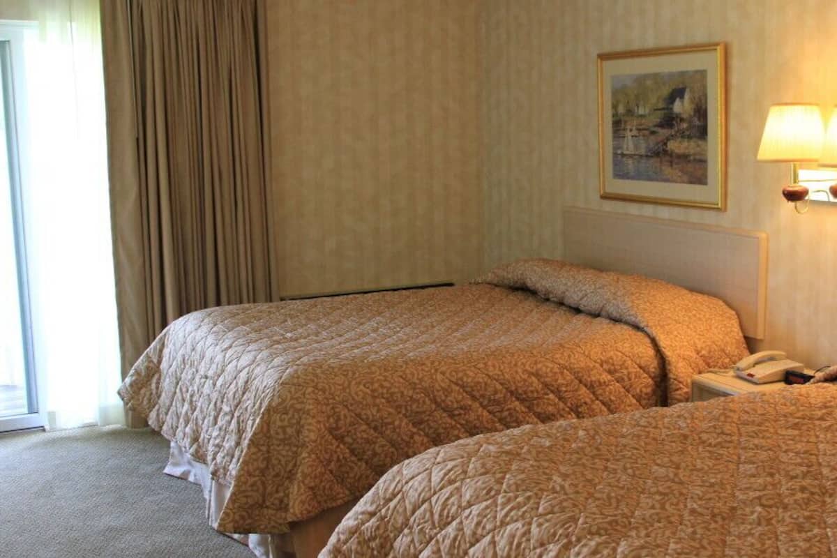 A hotel room with two beds, a painting on the wall, and a lamp.