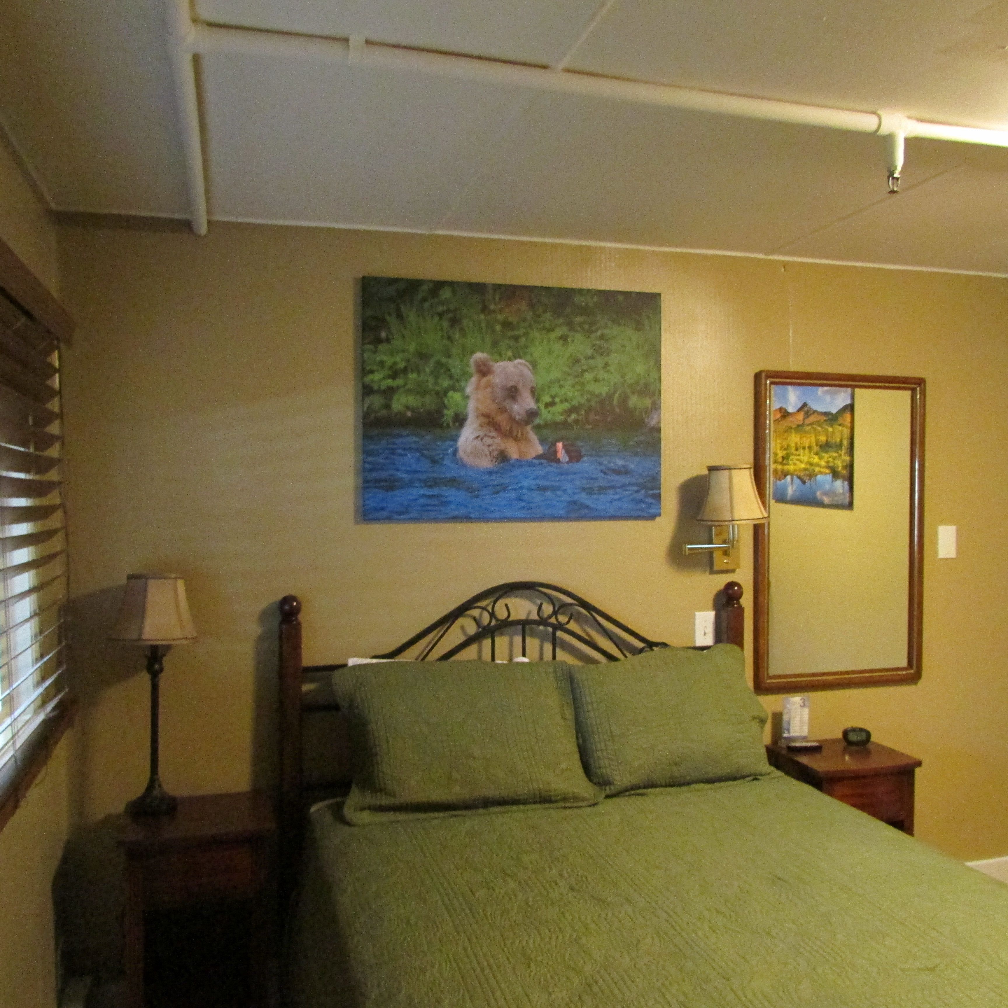 A bedroom with a bed, a nightstand, a lamp, a painting of a bear, and a mirror.