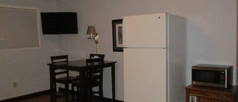 A compact room with a bed, a small table with chairs, a refrigerator, a microwave, and a TV on the wall.