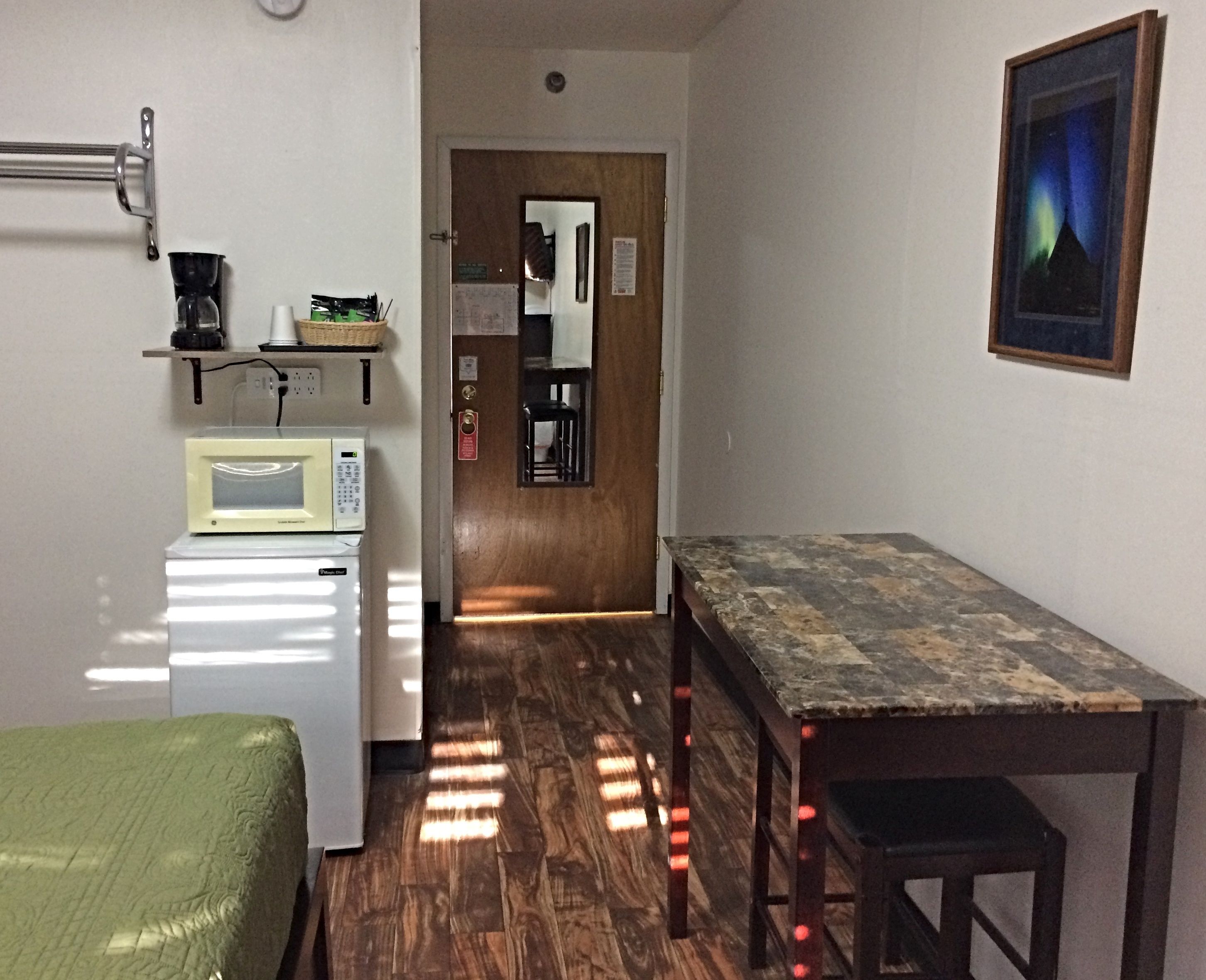 Una habitación compacta con kitchenette, una cama, una mesa y un cuadro en la pared.