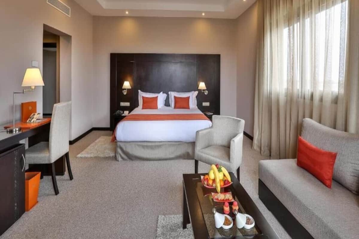Habitación de hotel con una cama grande, un escritorio con lámpara, un sofá y una mesa de centro con fruta.