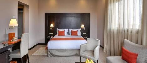 A hotel room with a large bed, a desk with a lamp, a sofa, and a coffee table with fruit.