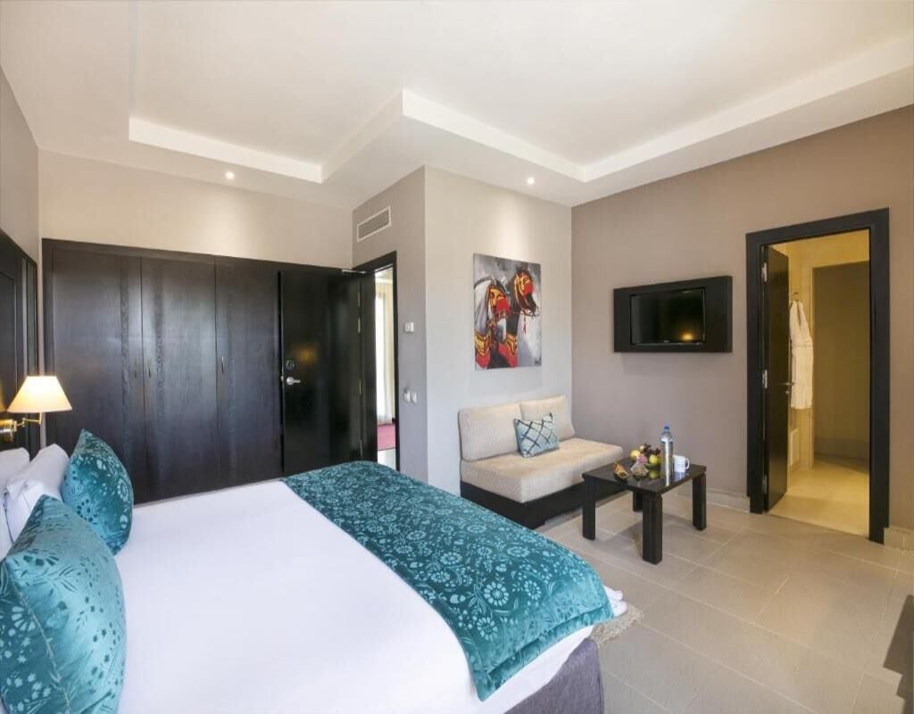 Quarto de hotel moderno com uma cama grande, um sofá, uma TV e um quadro na parede.