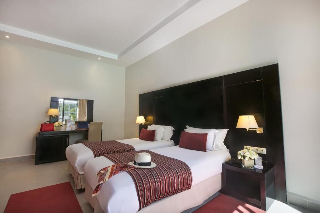 A hotel room with two beds, a desk, and a nightstand with lamps.