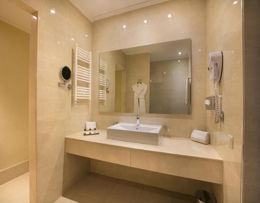 A modern bathroom with a large mirror, a sink, a towel rack, and a shower area.