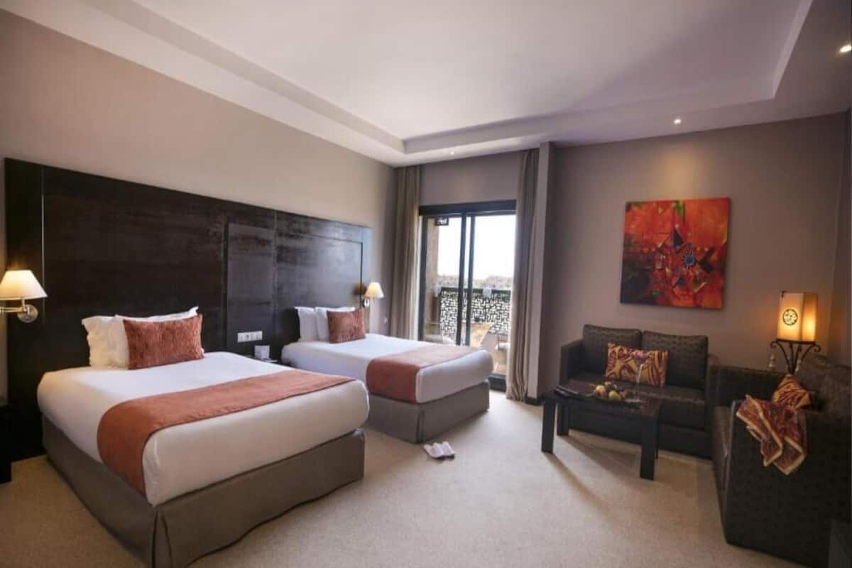 Habitación de hotel con dos camas, un sofá y un ventanal grande.