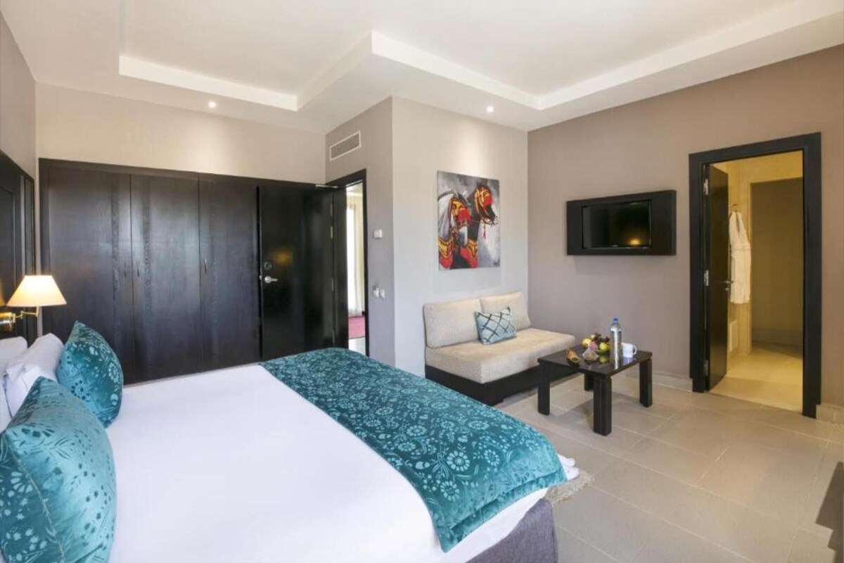 A hotel room with a bed, a sofa, a TV, and a bathroom visible through an open door.