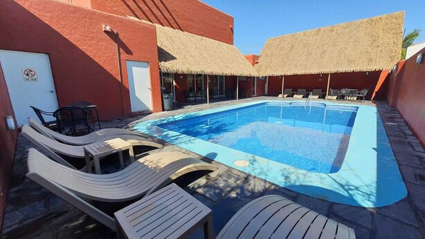 Una piscina con sillas de descanso y mesas, rodeada de edificios con techos de paja.