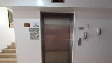 Een lift met een digitaal scherm, een brandveiligheidssignaal en een telefoon aan de muur.