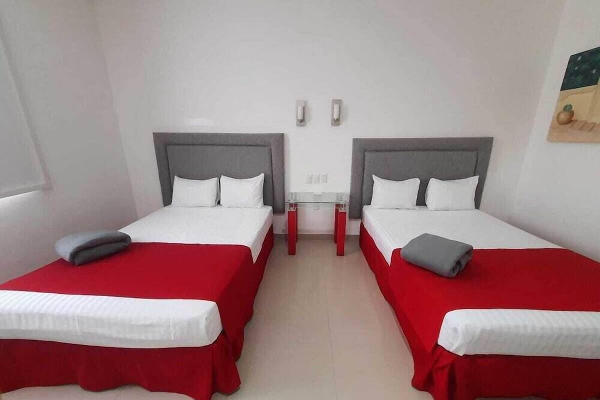 A hotel room with two beds, each with a red bedspread and white linens, and a grey headboard.