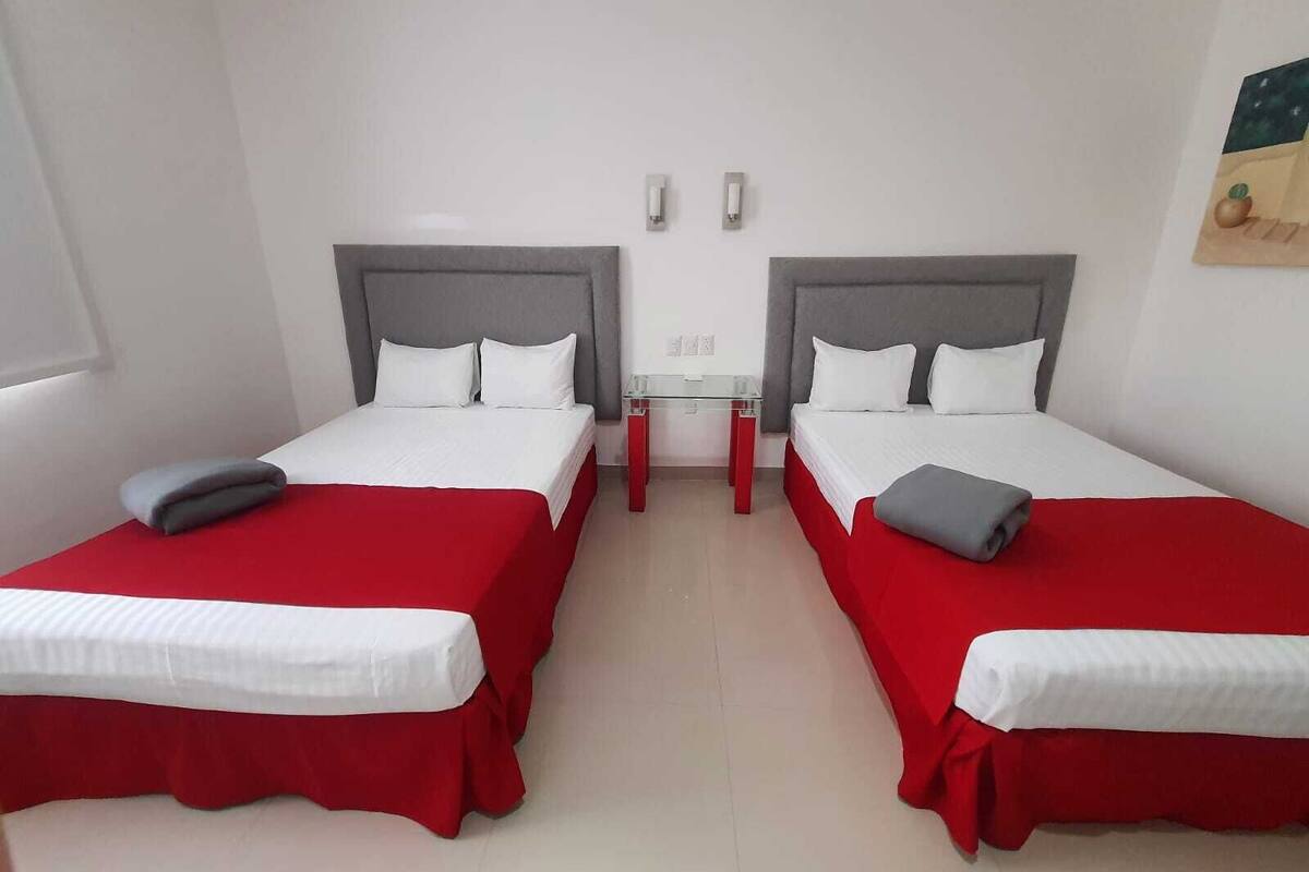 A hotel room with two beds, each with a red bedspread and white linens.