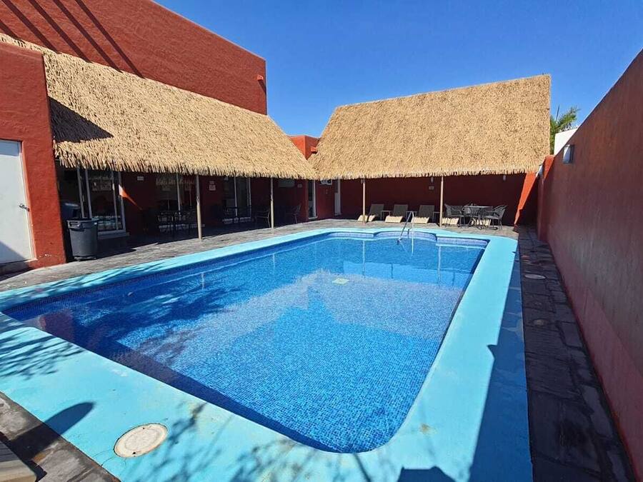 Piscina com borda azul, rodeada por edifícios vermelhos e estruturas com telhados de palha.