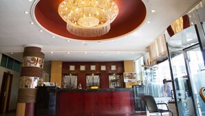 A hotel lobby with a grand chandelier, a reception desk, and a glass wall offering a view of the outside. - Jupiter International Hotel Bole (Addis Ababa)
