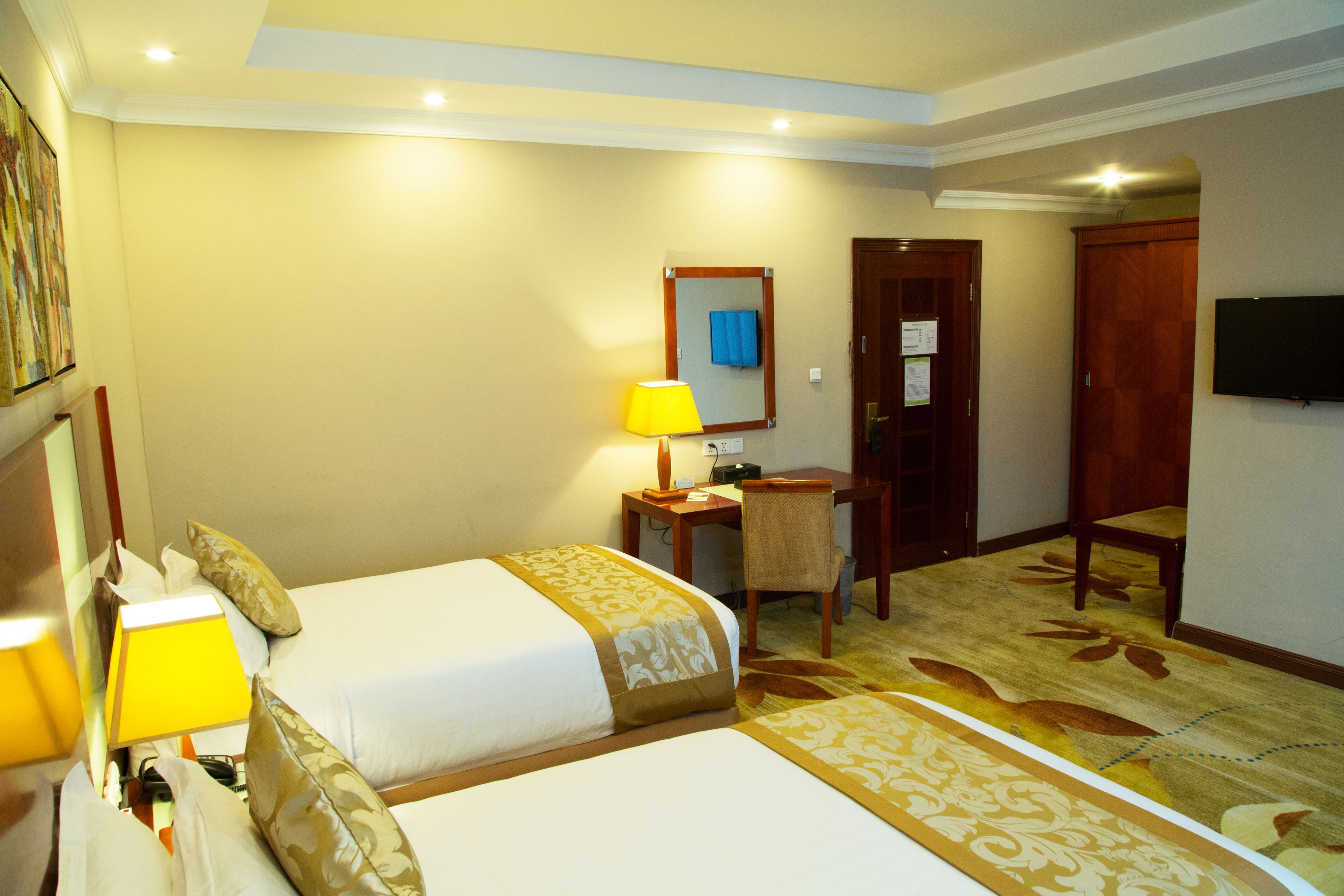 A hotel room with two beds, a desk, a chair, a lamp, a mirror, and a television.